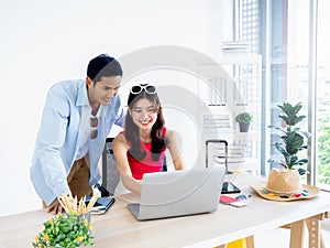 Happy Asian couple, young woman and man using laptop computer on desk together.