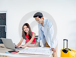 Happy Asian couple, young woman and man using laptop computer and map together.