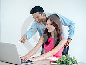 Happy Asian couple, young woman and man using tablet and laptop computer together.