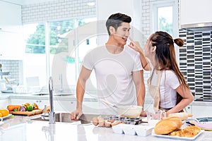 Happy Asian couples cooking and baking cake together in kitchen room. Man and woman looking to tablet follow recipe step at home.