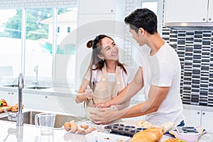 Happy Asian couples cooking and baking cake together in kitchen room. Man and woman looking to tablet follow recipe step at home.