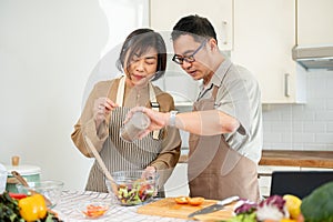 Happy Asian couples, husband and wife, are cooking a healthy salad bowl in the kitchen together