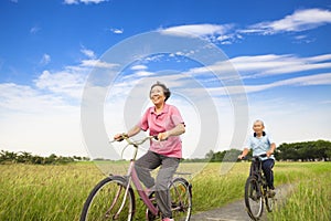 Happy Asian elderly seniors couple biking in farm