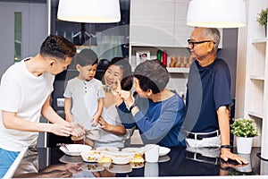 Happy Asian extended family preparing food and feeding a child at home full of laughter and happiness.