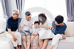 Happy Asian extended family sitting on sofa together, posing for group photos.