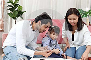 Happy Asian family. Chubby little girl daughter drawing together with father and mother in living room. Parents spend time with