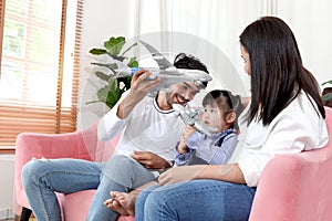 Happy Asian family. Chubby little girl daughter playing airplane toy with father and mother in living room. Kid and parents spend