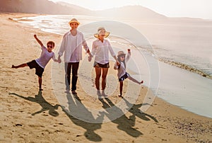 Happy asian family at consisting father, mother, son and daughter having fun on summer vacation on the beach with sunrise