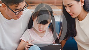 Happy Asian family dad, mom and daughter using computer tablet technology sitting sofa in living room at house. Self-isolation,