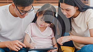 Happy Asian family dad, mom and daughter using computer tablet technology sitting sofa in living room at house. Self-isolation,