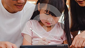 Happy Asian family dad, mom and daughter using computer tablet technology sitting sofa in living room at house. Self-isolation,