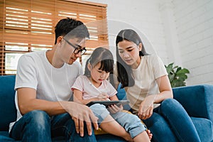 Happy Asian family dad, mom and daughter using computer tablet technology sitting sofa in living room at house. Self-isolation,