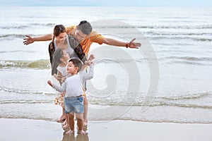 Happy asian family dad and mom with their children boy and girl raising hands with happy smiling face while standing on sandy