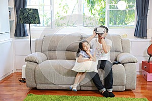 Happy Asian family, father and daughter playing virtual reality goggles on the sofa in the living room with happy smiling face