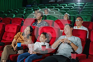 Happy Asian family of father, mother, daughter, and grandmother cherishes weekend moments at the cinema, sharing joy and