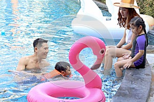 Happy Asian family, father mother daughter and son enjoy outdoor activity at pool, kid and parent swimming with pink flamingo