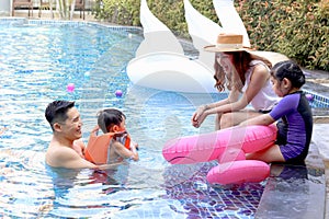 Happy Asian family, father mother daughter and son enjoy outdoor activity at pool, kid and parent swimming with pink flamingo