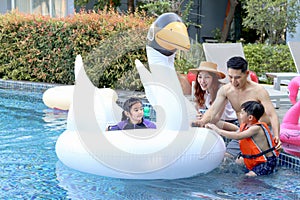 Happy Asian family, father mother daughter and son enjoy outdoor activity at pool, kid and parent swimming with white swan plastic