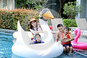 Happy Asian family, father mother daughter and son enjoy outdoor activity at pool, kid and parent swimming with white swan plastic