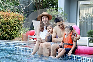 Happy Asian family, father mother daughter and son enjoy outdoor activity at swimming pool, kid and parent sitting by blue water