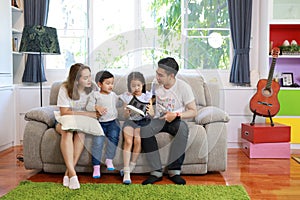 Happy Asian family, father, mother, son and little girl playing virtual reality goggles on sofa in living room together. Dad and