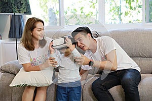 Happy Asian family, father, mother and son playing virtual reality goggles on the sofa in the living room with happy smiling face