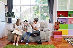 Happy Asian family, father, mother and son playing virtual reality goggles on the sofa in the living room with happy smiling face