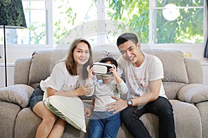 Happy Asian family, father, mother and son playing virtual reality goggles on the sofa in the living room with happy smiling face