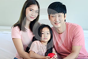 Happy Asian family having fun in bedroom. Father, mother and daughter girl hugging each other to show warm love, mom and dad,