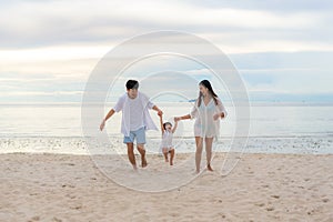 Happy Asian family holidays during joyful father, mother and daughter running together along summer sunset sea. Happy family