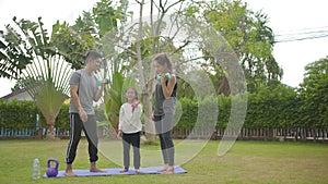 Happy asian family with kid doing weight training exercises on yoga mat in the grass park at the day