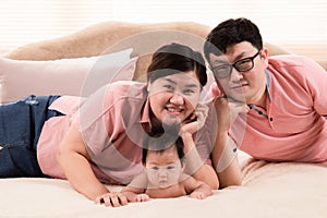 Happy asian family laying down and taking pictures together in bedroom. parents and little daughter looking at camera posing for