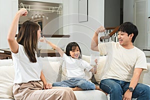 Happy Asian family, mother and father cheering little 6 year old daughter drinking milk from glass, raised arm muscles and fist