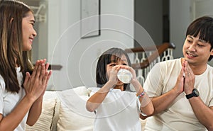 Happy Asian family, mother and father clapping hands cheering their little 6 year old daughter drinking milk from glass with