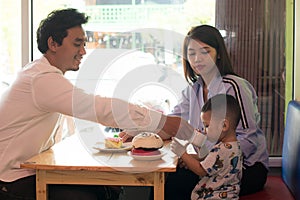 Happy asian family, with one todler spending time together inside bakery store and cafe eating cake