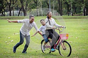 happy asian Family, parents and their children riding bike in park together. father pushes  mother and son on bicycle having fun photo