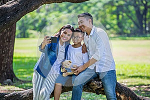 happy asian Family, parents and their children taking selfie in park together. father, mother ,son sitting on branch of big tree