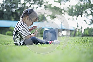 Happy asian family picnic. Daughters playing mobile phones and laptops having fun together while sitting alone on sunny day