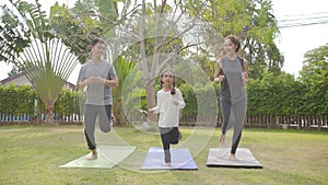 Happy asian family playing with children doing yoga exercises on grass in the park at the day time