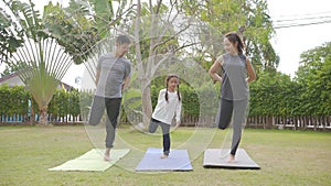 Happy asian family playing with children doing yoga exercises on grass in the park at the day time