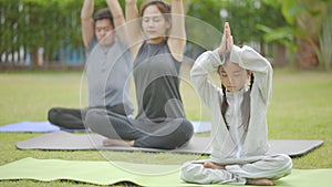 Happy asian family playing with children doing yoga exercises on grass in the park at the day time