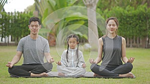 Happy asian family playing with children doing yoga exercises on grass in the park at the day time