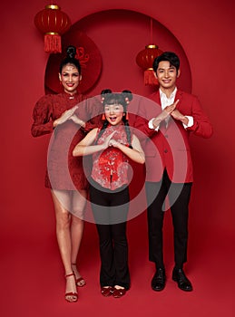 Happy asian family in red casual attire with gesture of congratulation greeting happy new year 2024 on Decoration traditional red