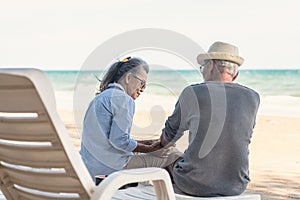 Happy Asian family, senior couple sitting on chairs with backs on beach travel vacation talking together