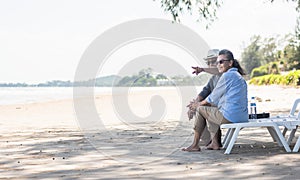 Happy Asian family, senior couple sitting on chairs with backs on beach travel vacation talking together