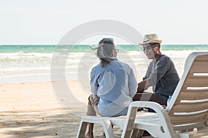 Happy Asian family, senior couple sitting on chairs with backs on beach travel vacation talking together