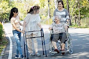 Happy asian family,senior woman, disabled grandmother with walker and wheelchair, daughter,teen granddaughter enjoying a walk in