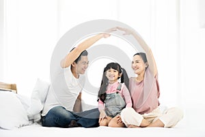 Happy asian family sitting on bed in bedroom together and making the home sign