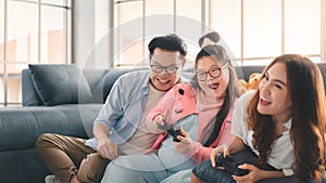 Happy asian family sitting on floor and playing video games with their daughter down syndrome child in living room at morning time