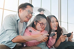 Happy asian family sitting on sofa and playing video games with their daughter down syndrome child in living room at morning time